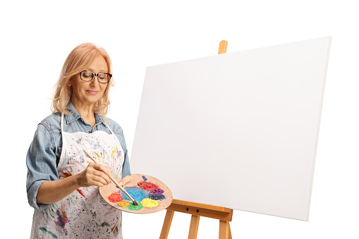 Woman holding a painting brush and palette with acrylic paint next to a blank canvas isolated on white background