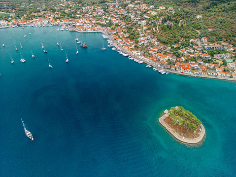 Aerial view of sailboats anchored in a beautiful bay of Vathi, Ithaca, Greece. There are small, traditional mediterranean houses near waterfront. It's a beautiful sunny summer day, the sea is blue, green and turquoise. There is a small island in the middle of the bay.