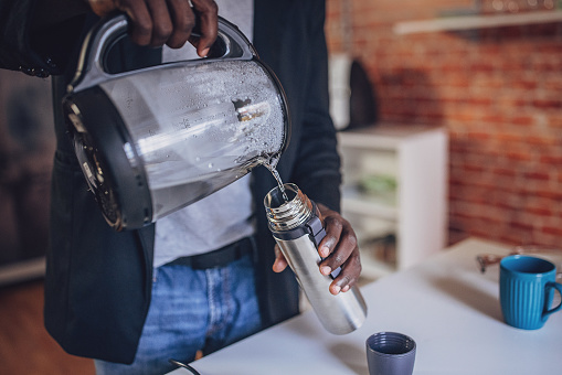 African American man casually dressed, making coffee in a chic kitchen with a brick wall background.