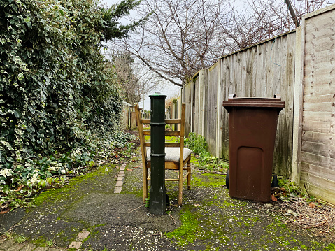 Broken chair left by a brown wheelie bin in an alley