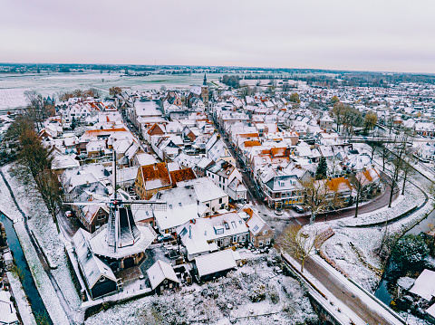Hattem aerial view during a cold winter morning with snow on the rooftops seen from above. The town Hattem is bordering the forests of ‘De Veluwe’ on one side and lies along the IJssel river the other side, which can be seen in the background.