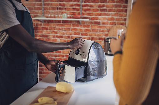 African American man and woman engaging in cooking with an air fryer in a kitchen adorned with a brick wall.