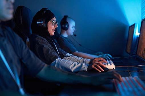 Side view portrait of Muslim young woman playing video games in blue neon light, copy space