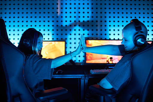 Back view of two young women playing video games and celebrating victory in blue light