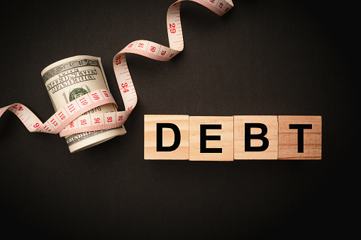 The public debt of the United States is considerable and the debt ceiling must be increased. A tape measure was wound around a US dollar bill with a green up arrow and a red down arrow percentage.