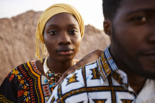 Closeup portrait of Black young couple outdoors in desert landscape with young woman leaning on man and looking at camera, copy space