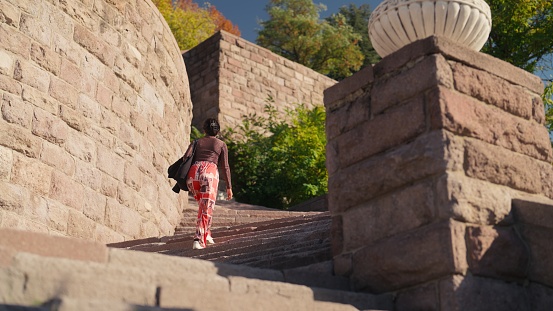 A multi-racial female tourist is visiting an old antient town and climbing up stairs.