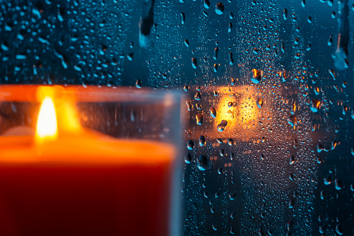 Drops of water on window glass and burning candle
