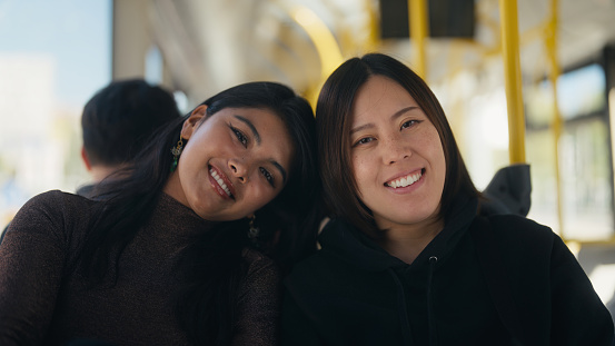 A portrait of two multi-ethnic female tourist friends on a bus in a city.