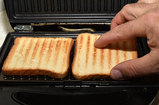 A man's hand removes ready-cooked toast and bread from the grill.