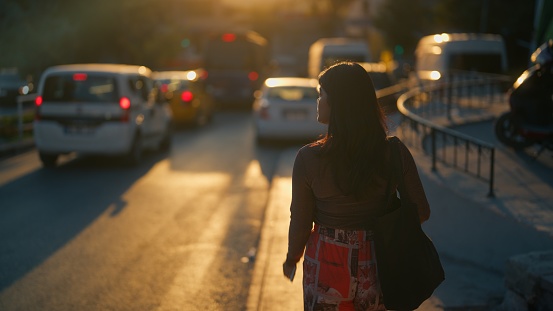 A rear view video of a multi-ethnic female tourist walking in the street during sunset during her travel.