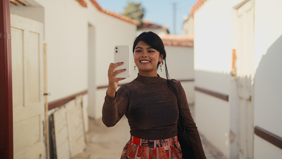 A multi-racial female tourist is visiting an old ancient town and taking photos and videos with her mobile smart phone.