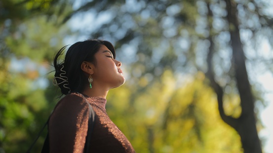 A portrait of a multi-racial young beautiful woman with her eyes closed in a public park in summer.