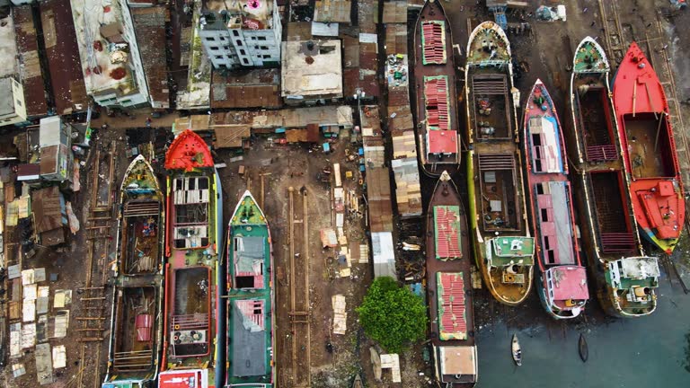 Aerial: rusty abandoned cargo ships for repair at dockyard beside slum community in Asia