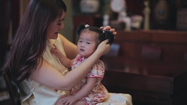 Chinese New Year Mother tying hair for baby girl in living room