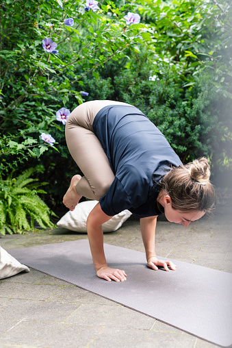 Slim woman practicing yoga bakasana or crow pose in a beautiful garden. Concept of a healthy lifestyle, women's wellness, and active recreation.