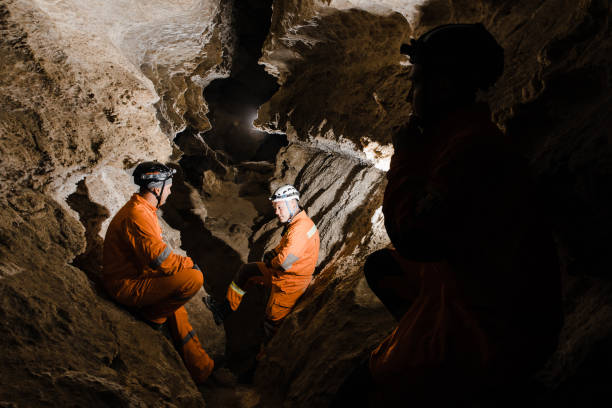 istock Three men, strong physique, explore the cave. Men dressed in special clothes to pass through the cave and stopped, looking at the map 1852028289