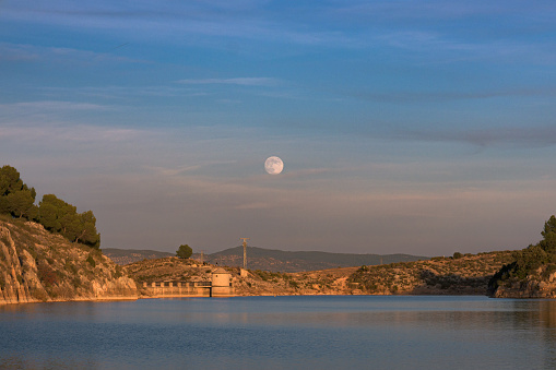 The moon in the background over a lake at dusk