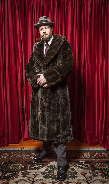 Standing Bearded Man Wearing Fedora, Fur Coat, Pipe in Mouth "Standing Bearded Man Wearing Fedora, Fur Coat, Pipe in MouthThe man is standing on an ornate carpet in front of a red curtain. He holds a pipe in his mouth, and his hands are clasped in front of him." leather clasp stock pictures, royalty-free photos & images