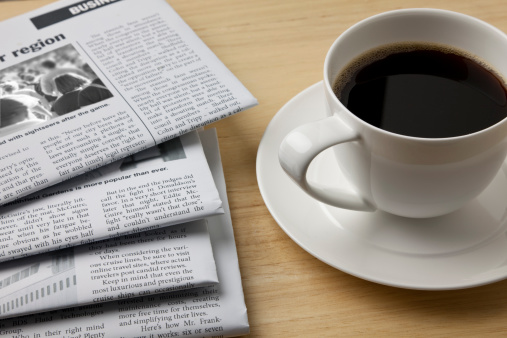 A newspaper and a cup of coffee on a wooden table.Click on the banner below to see more photos like this.