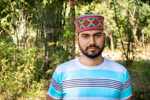 Outdoor portrait of a young man from Himachal Pradesh with traditional Himachali cap looking at the camera with a smile.