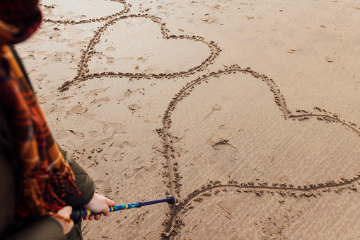 A high angle view of an unrecognisable women drawing a heart in the sand as she enjoys a walk with friends of hers in Bamburtgh in the North East of England.