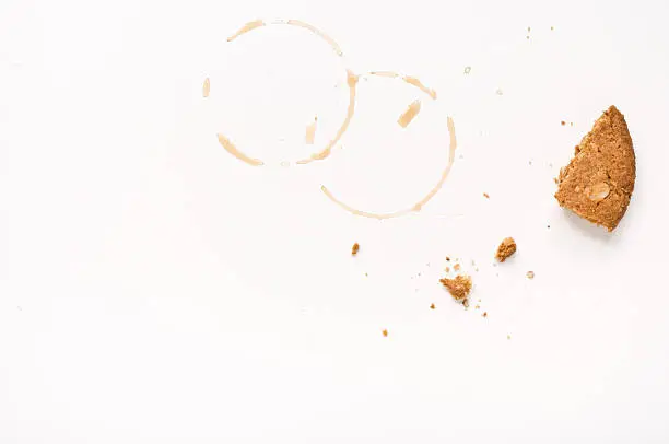 Cookie crumbs and coffee stains on white table.