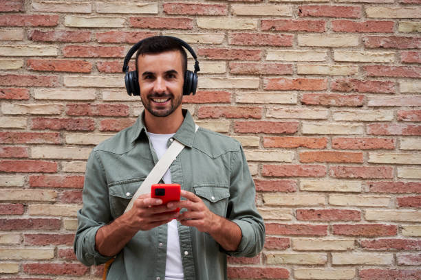 istock Caucasian man looking at camera smiling while using phone to send online messages and listen music. 1852118365