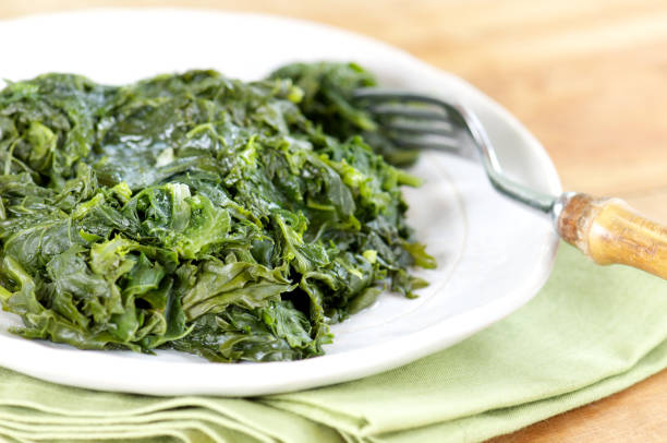 A plate of Southern style braised greens next to a fork Plate of Southern-style mixed braised collards and kale with fork and napkin braised stock pictures, royalty-free photos & images