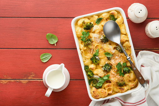 Casserole Mac and cheese. Baked Mac and cheese with broccoli, cream sauce and parmesan on red old rustic wooden background. Healthy or baby food. American Casserole Top view. Copy space.