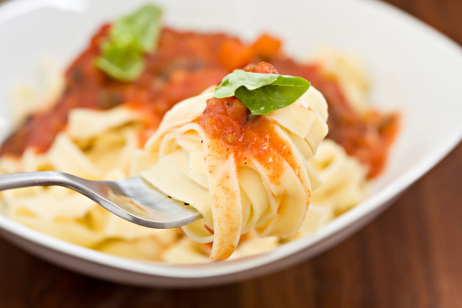 A high angle close up of some fresh fettuccine with some marinara sauce wrapped on a fork.