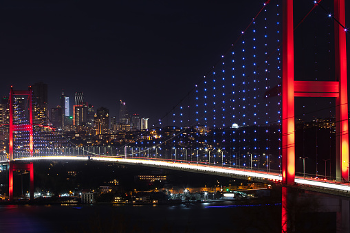 View of The July 15 Martyr's Suspension Bridge on Bosphorus straits and high rise office buildings in the background at night seen from the asian side of Istanbul, Turkey.