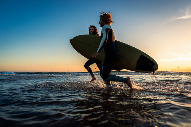istock Two surfers with surfboard prepares to hit the waves at sunset. 1852155145