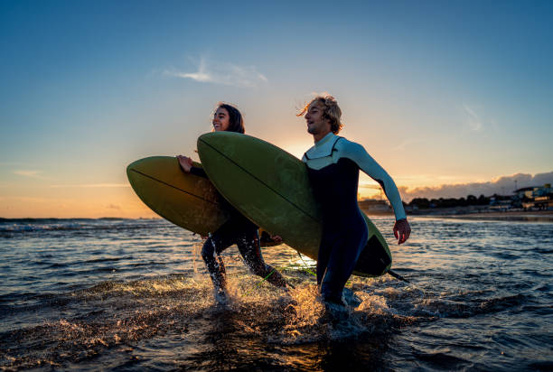 istock Two surfers with surfboard prepares to hit the waves at sunset. 1852155148