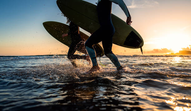 istock Two surfers with surfboard prepares to hit the waves at sunset. 1852155150