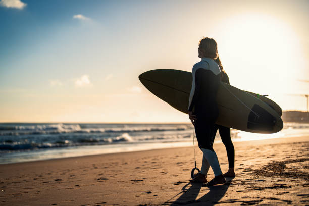 istock Two surfers with surfboard prepares to hit the waves at sunset. 1852156757