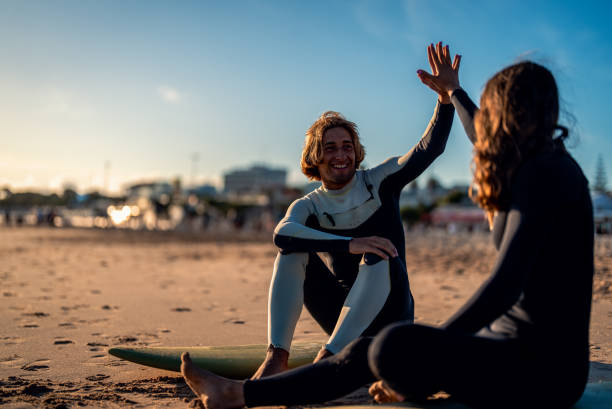 istock Two surfers with surfboard sitting on beach resting after surfing at sunset. 1852157277