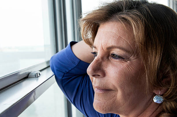 istock Senior woman looking through a window 185217151