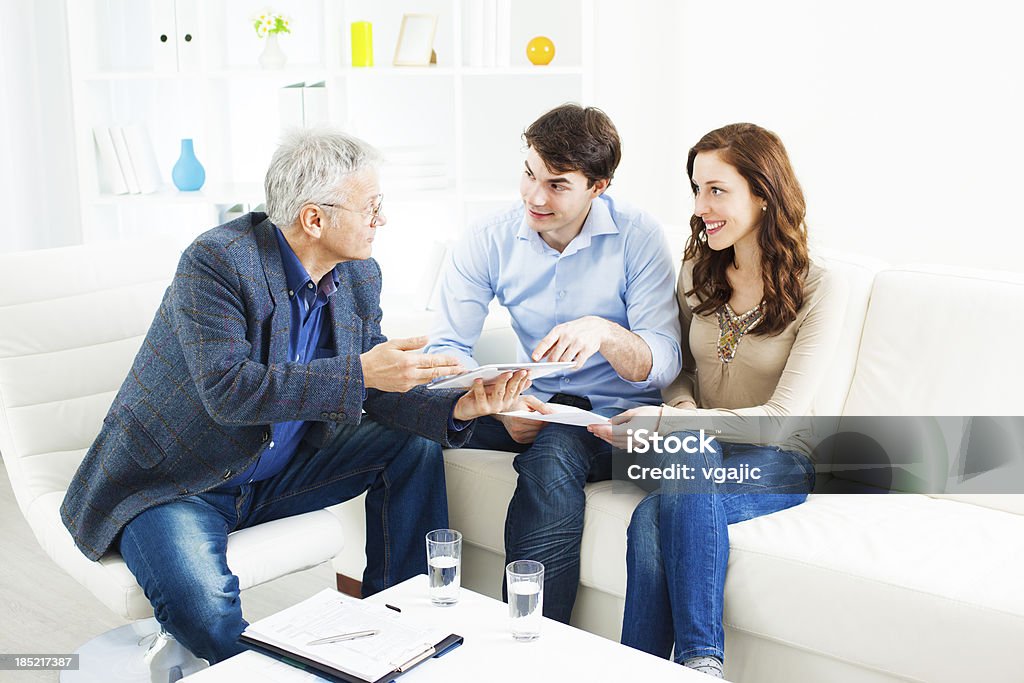 Couple Meeting With Financial Advisor Young Couple Meeting With Senior Financial Advisor presenting new bank offers and investments on digital tablet PC. Senior Financial Advisor pointing with hand to some new offers. Digital Tablet Stock Photo