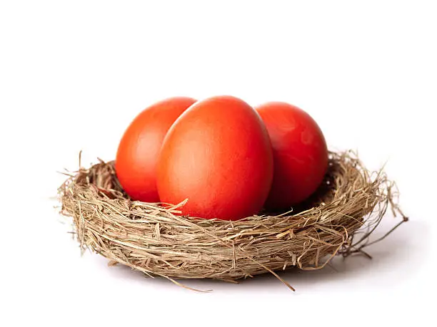 Red Easter eggs in a straw nest closeup with white background and copy space