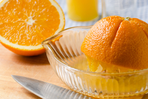 Navel oranges with a glass citrus reamer/juicer on a cutting board with a chef's knife and juice glasses in the background.Similar Images: