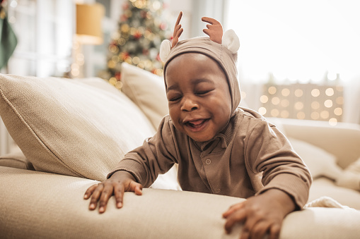 Little baby in reindeer costume crawling on sofa.