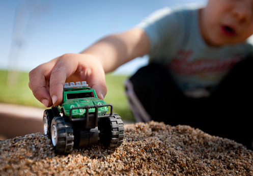 Boy playing with toy truck in the sand at the park