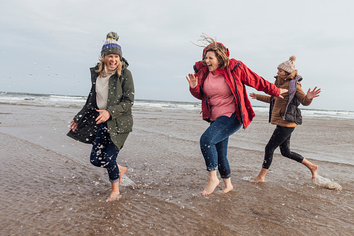 A close up view of a group of four women who are enjoying a coastal walk in Bamburgh in the North East of England. They have decided to go barefoot and dip their toes in the sea for a little bit of fun. They are splashing about and kicking water over each other.