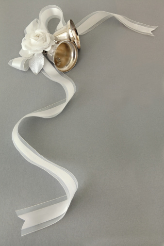 Silver wedding bells tied with a white ribbon and adorned with pearls and flowers on a silver background