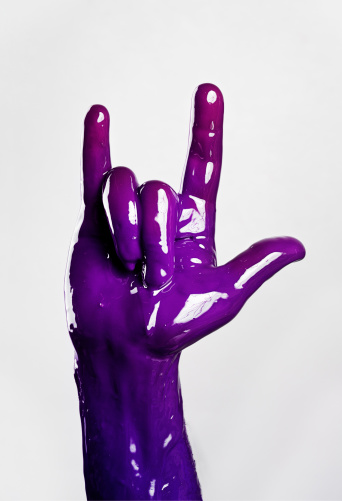 Hand covered of liquid paint making a punk sign.