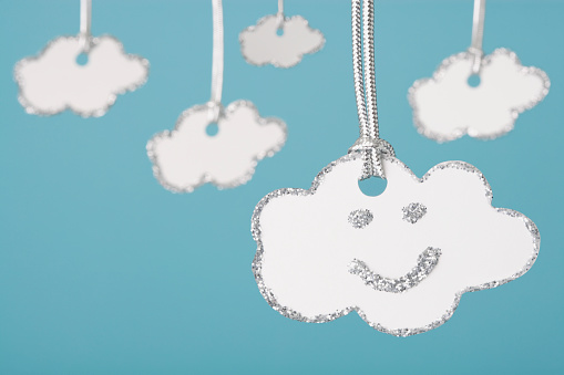 Every cloud has a silver lining... fun shot of well known proverb, white card clouds with silver glitter edges hanging from shiny silver cord.