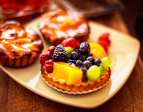 a fruit tarts and two apricot tarts on a dessert plate with extra raspberries and blueberries over a wooden surface