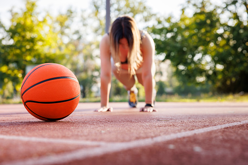 Low angle view of fit young woman in sportswear doing push ups on an outdoor basketball court as morning workout routine