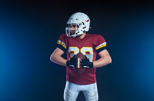 portrait of intent high school or college athlete with black white and yellow uniform holding american football isolated on white background